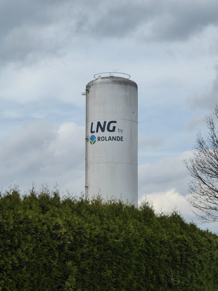 Vertical LNG storage silo by Rolande surrounded by greenery and cloudy sky.
